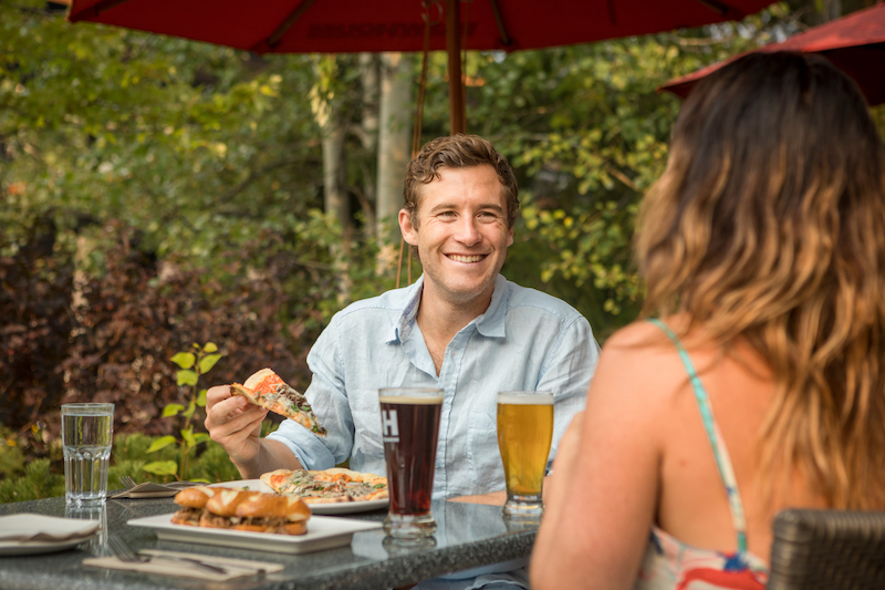 couple eating food at outdoor restaurant in whistler blackcomb with two beers and nice weather